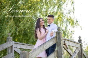 Couple sur un pont en bois sous un arbre, photos de couple, robe rose, nœud papillon bleu, chemise blanche, saule pleureur